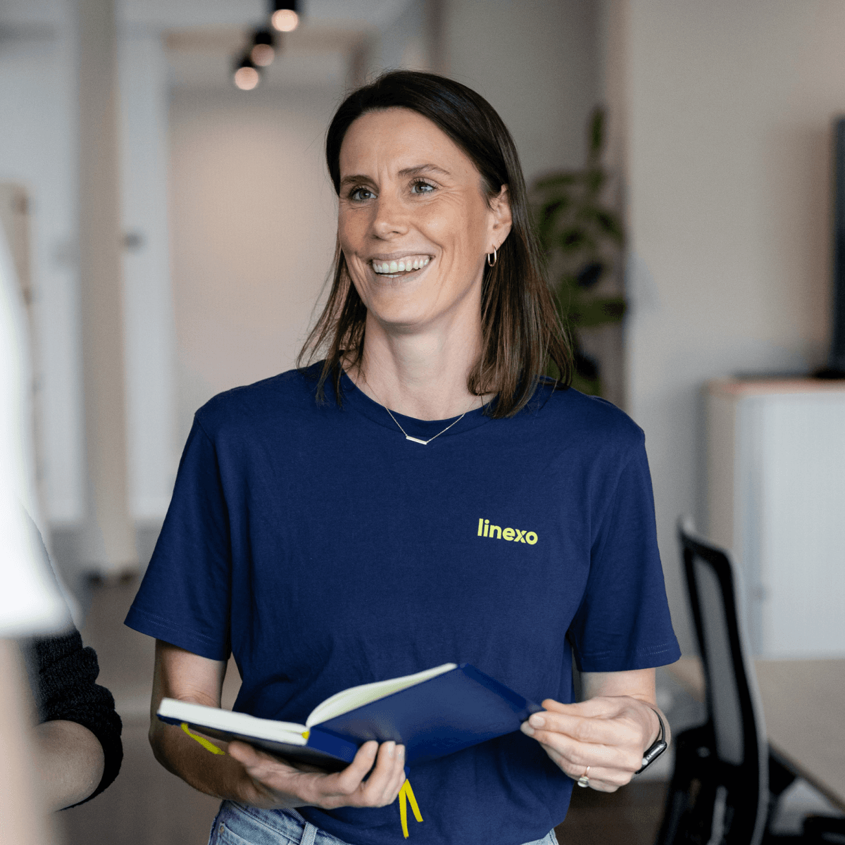 Edda Reinholz, Teamleiterin Marketing Services, schaut lächelnd mit einem Notizbuch in der Hand in die Kamera.