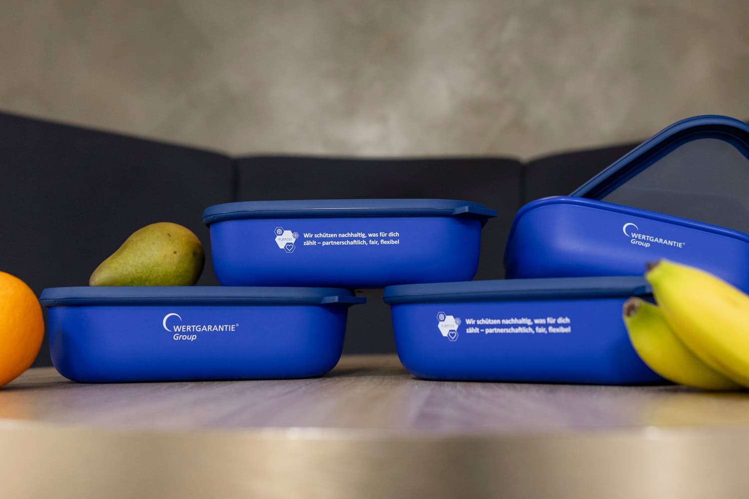 Vier Lunchboxen sind neben Obst übereinander gestapelt