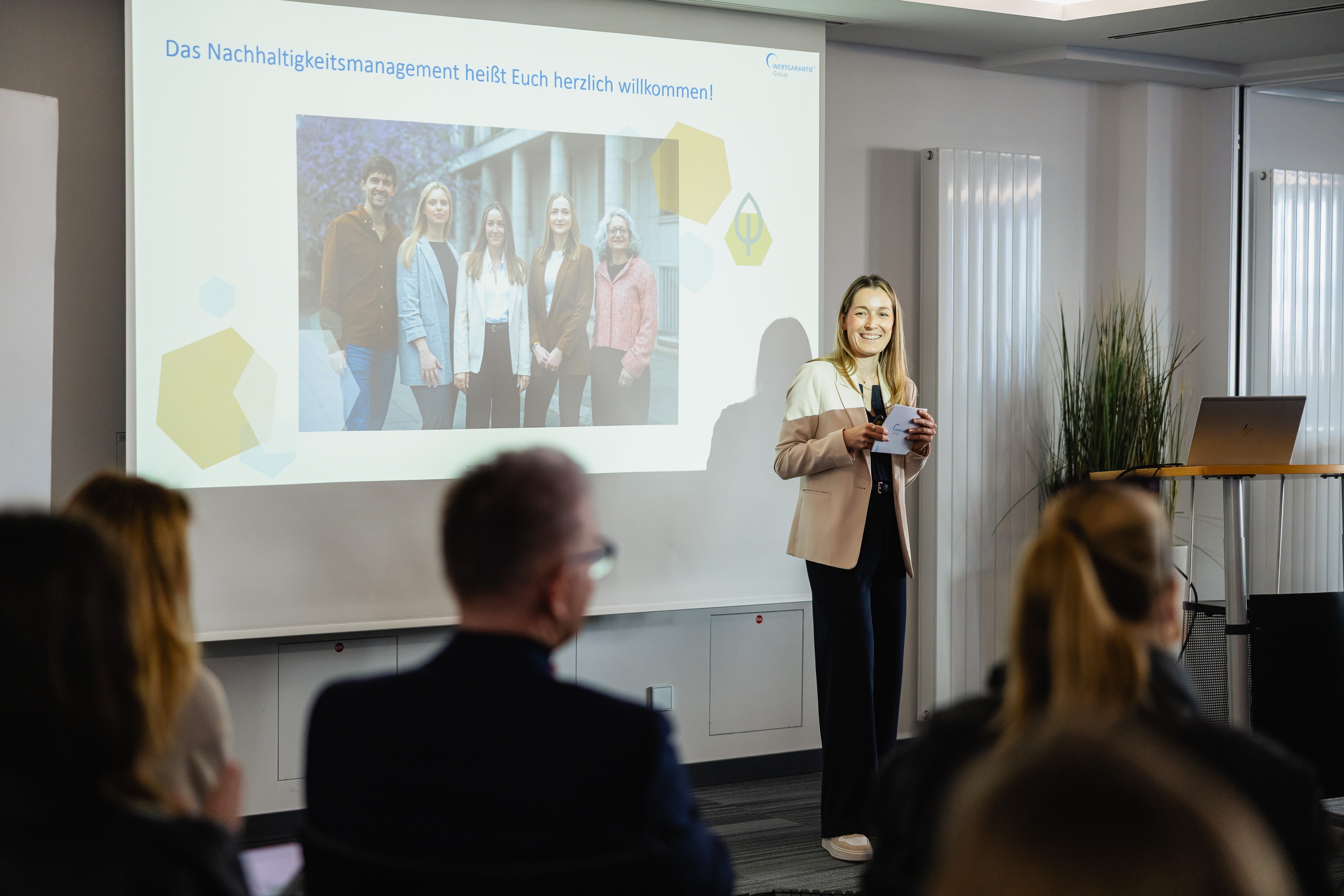 Nina Ruhnow, Abteilungsleiterin Nachhaltigkeit, referiert mit Präsentation im Hintergrund beim Kick-Off-Event zur Nachhaltigkeitsstrategie der WERTGARANTIE Group.