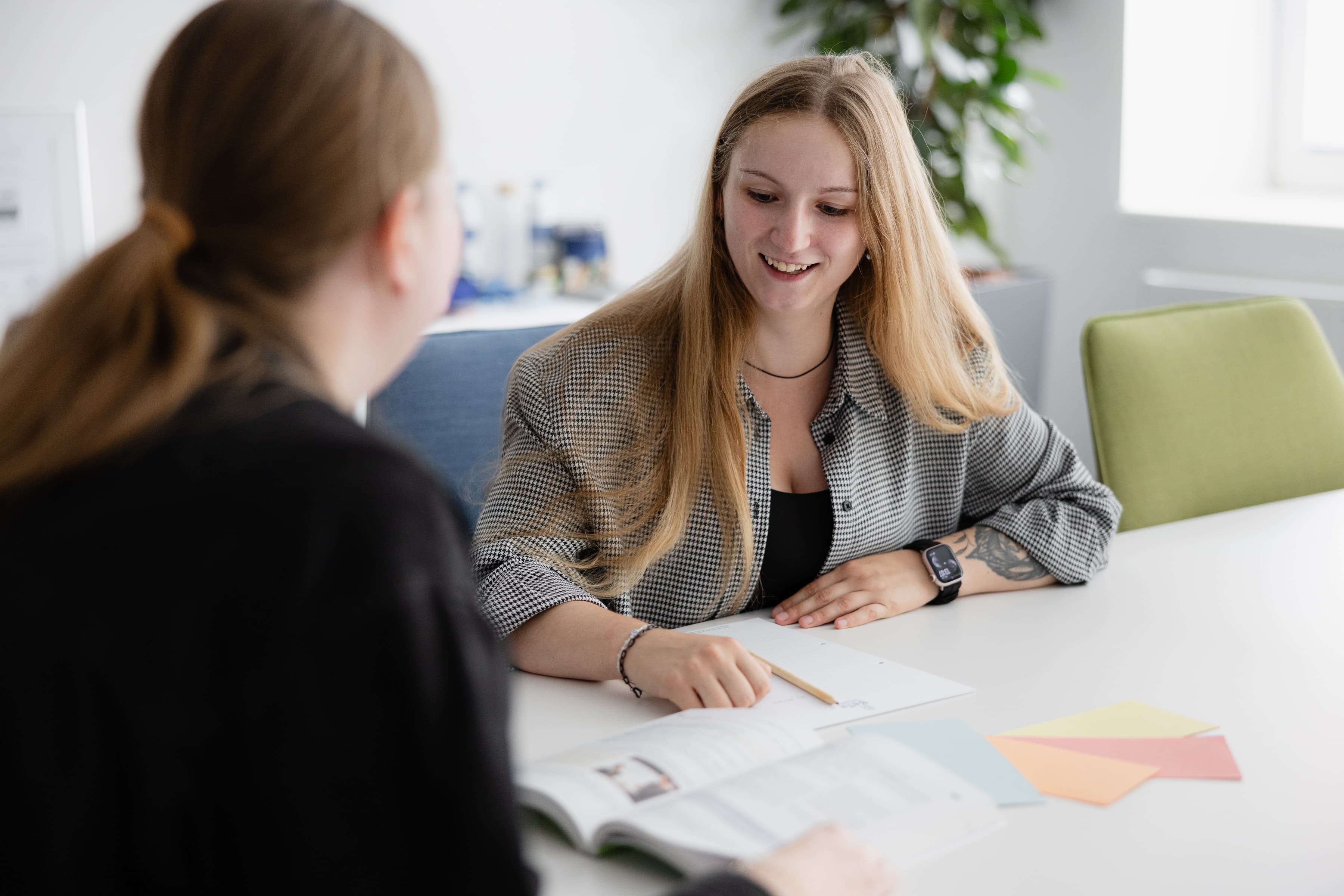 Zwei Auszubildende der WERTGARANTIE Group sitzen ein einem Tisch und schauen sich Lehrmaterial an.