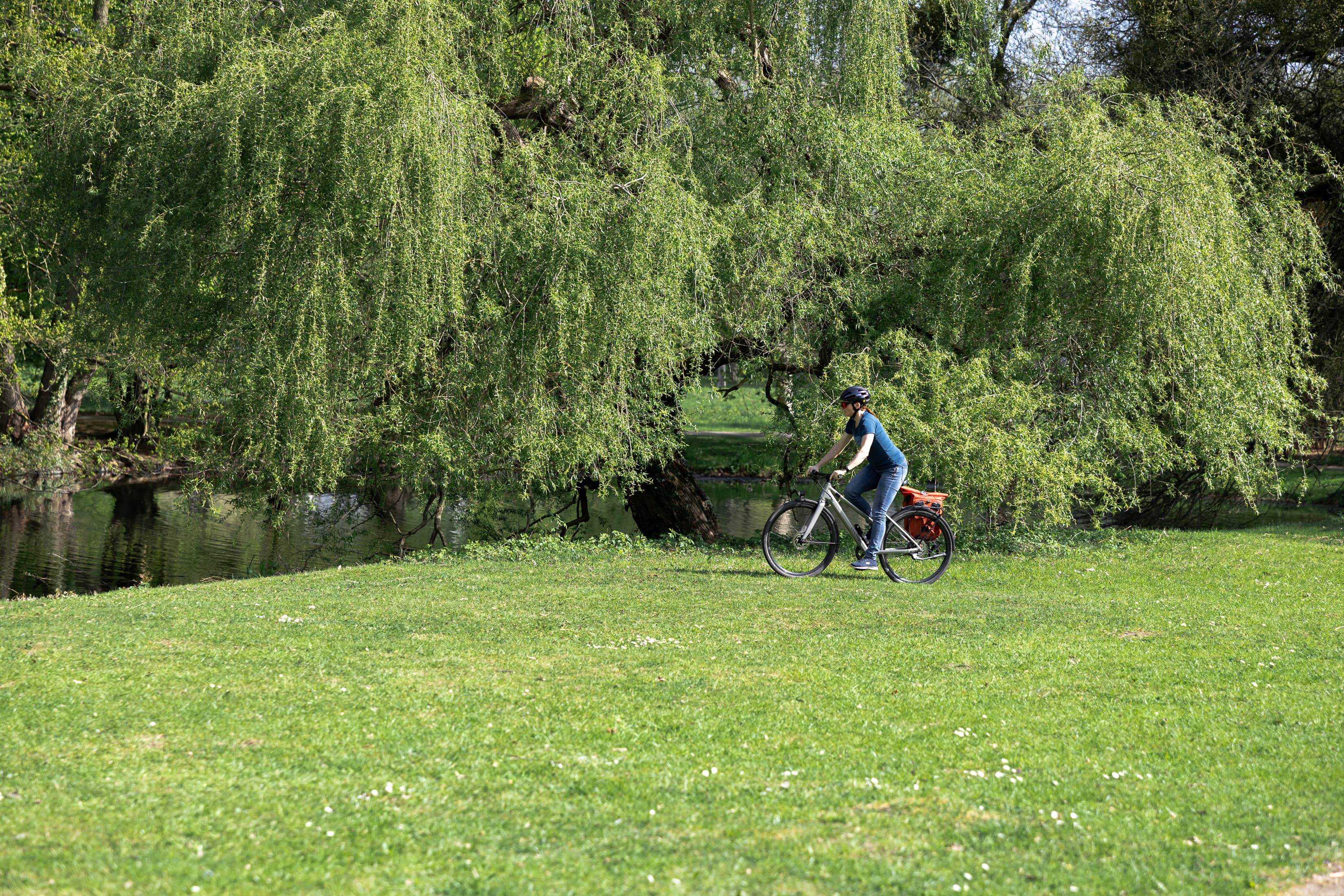 Eine Mitarbeiterin der WERTGARANTIE Group steht mit ihrem Fahrrad im Grünen im Georgengarten Hannover.