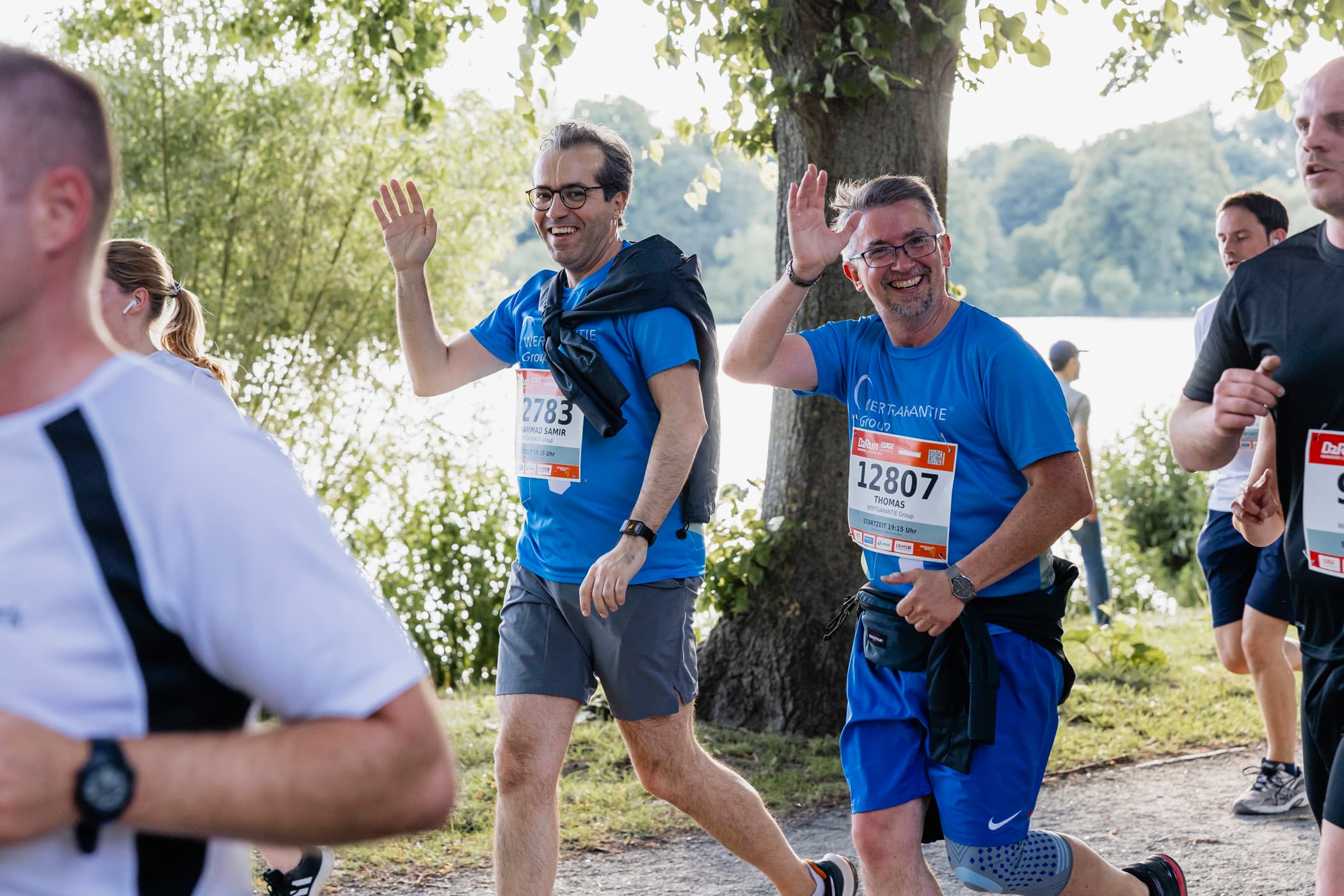 B2Run Mehrere Leute laufen bei einem Wettbewerb mit, zwei Kollegen winken in die Kamera