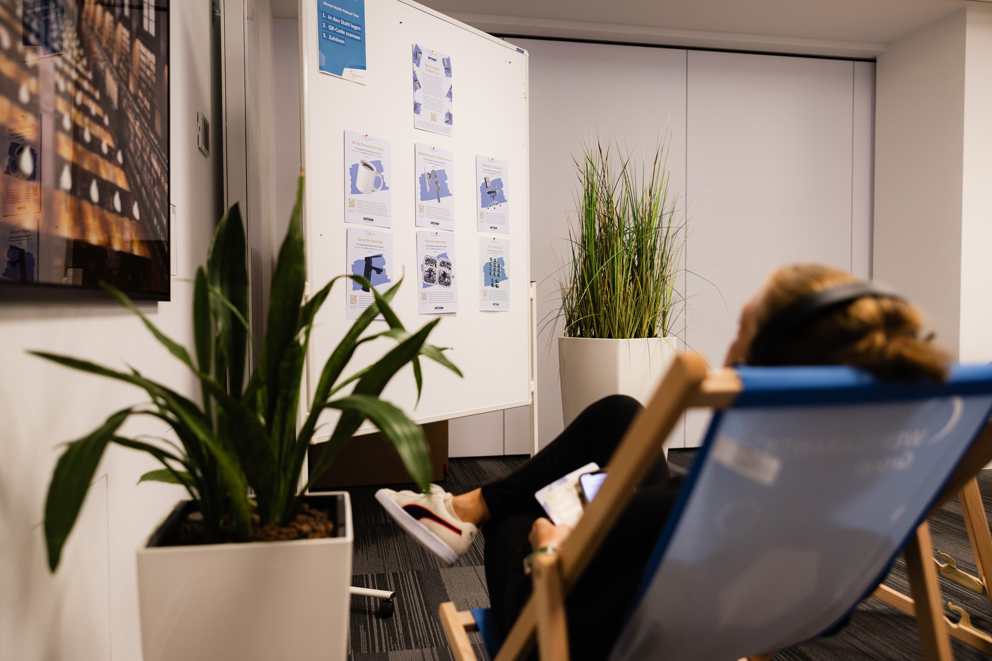 Mental Health Audio Ausstellung Eine Mitarbeiterin liegt mit Kopfhörern auf einem Liegestuhl und hört sich die Mental Health Audio Ausstellung bei den Gesundheitstagen an.
